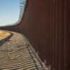 Long view of a steel border wall under clear skies, emphasizing solitude and division.