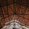 View of architectural wooden roof trusses inside an old factory with exposed ceiling and natural light.