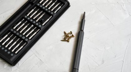 Close-up of a precision screwdriver kit with various bits and screws on a light textured background.