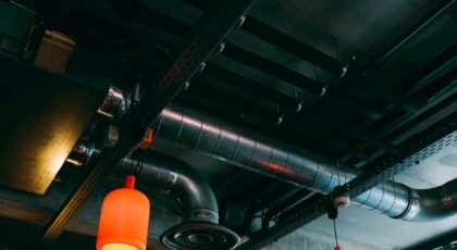 Low-angle view of a modern industrial ceiling featuring ducts and red lamps.