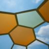 Low angle view of colorful hexagonal panels forming a geometric roof with blue sky and clouds.