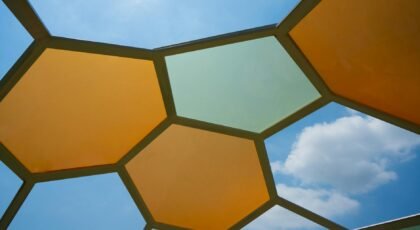 Low angle view of colorful hexagonal panels forming a geometric roof with blue sky and clouds.