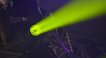 Close-up of a vivid neon spotlight emitting a green beam, part of modern stage lighting equipment.