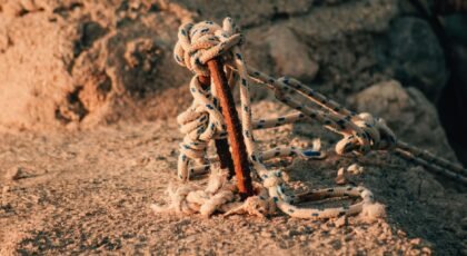 Close-up of a nautical rope tied to a rusty metal pole on a textured stone surface.