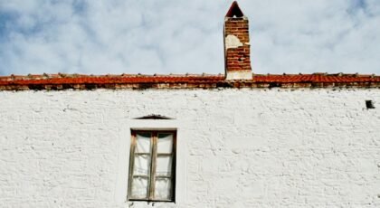 A historic whitewashed building with a red brick chimney set against a blue sky.