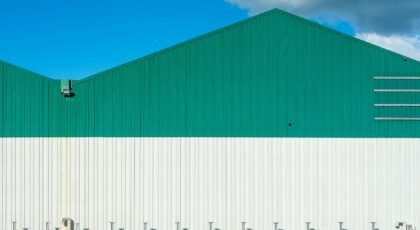 Green and white industrial warehouse under blue sky with cloud.