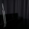 A close-up of a metal tuning fork standing on a reflective piano surface with dark background.