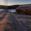 Abandoned barn next to a frozen lake with a sunset backdrop, creating a serene winter scene.