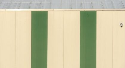 A minimalist industrial building facade featuring vertical green stripes and metal roof.