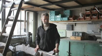 Bearded man working on metal piece in a rustic workshop setting.