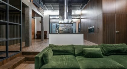 Spacious modern loft featuring an elegant green sofa, industrial decor, and sleek kitchen.