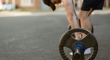 A young male athlete lifting a barbell outdoors on an urban street.