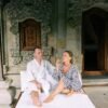 A couple in robes enjoy a relaxing moment outside a Balinese villa with ornate carvings.