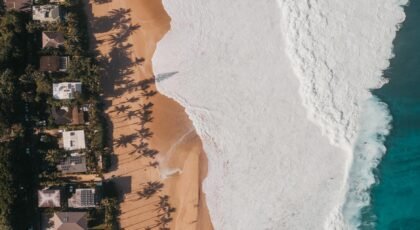A breathtaking aerial photo of a beachfront in Hawaii with waves crashing onto the sandy shore.