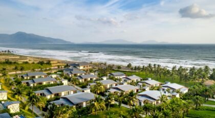 Aerial view of beachside villas with palm trees and ocean waves, perfect for travel and tourism.