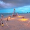 Beautiful beach dinner setup with lanterns glowing on a serene coastline during twilight.