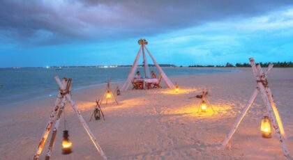 Beautiful beach dinner setup with lanterns glowing on a serene coastline during twilight.