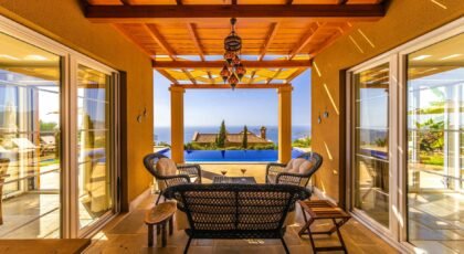 Relaxing patio at a luxury villa with sea view, featuring rattan furniture and infinity pool.