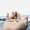 Close-up of hand holding shells with the serene Bali coastline in the background.