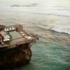 Aerial view of a luxurious cliffside resort in Bali, Indonesia, with ocean and swimmers below.