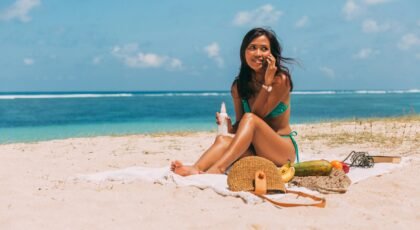 Woman relaxing on a sandy beach with picnic items, enjoying the sun and ocean view.