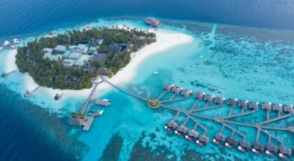 Stunning aerial view of a luxurious tropical island resort in the Maldives, featuring turquoise waters and overwater bungalows.