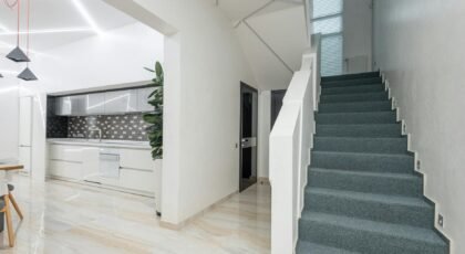 Stairway in corridor of spacious house near light kitchen with minimalist furniture and modern appliances