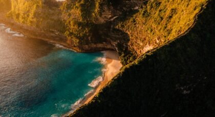 A breathtaking aerial view of Bali's cliffs and turquoise beach at sunset, highlighting nature's beauty.