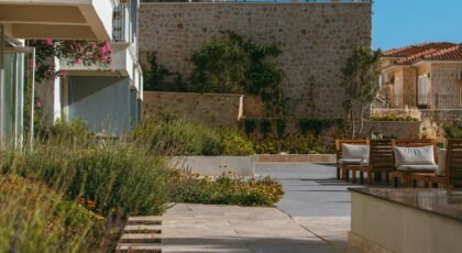 A sunny Mediterranean courtyard featuring rustic stone walls and wooden seating.
