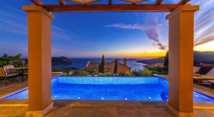 Stunning view of a luxury villa and infinity pool overlooking the sea at sunset.