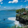 Stunning coastal view of Bali with a cliffside villa and lush palm trees under a clear blue sky.