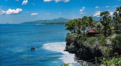 Stunning coastal view of Bali with a cliffside villa and lush palm trees under a clear blue sky.
