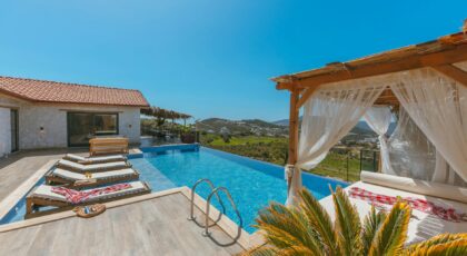 Elegant villa with an infinity pool, deckchairs, and cabana offering a panoramic hillside view.