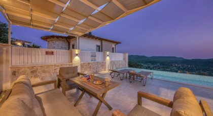 Cozy terrace with pergola overlooking mountains and infinity pool at sunset.