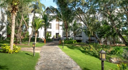 A lush pathway lined with palm trees leads to a luxurious villa, perfect for a relaxing getaway.