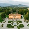 A stunning aerial view of a historic villa and gardens in Italy, surrounded by lush greenery.