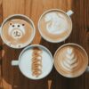 Four cups of creative latte art designs on a wooden table, showcasing intricate coffee art.