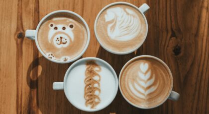 Four cups of creative latte art designs on a wooden table, showcasing intricate coffee art.