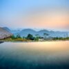 Clean water of pool located on tropical resort with wooden bungalows against silhouettes of mountain ridge on evening time in nature