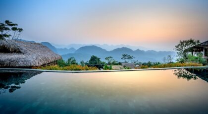 Clean water of pool located on tropical resort with wooden bungalows against silhouettes of mountain ridge on evening time in nature
