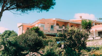 Charming Mediterranean villa nestled in vibrant, lush gardens under a clear blue sky.