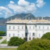 A grand villa surrounded by lush gardens and mountains near the Italian lake.