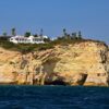 A stunning view of Algarve's sea cliffs with a villa on top, under a clear blue sky.