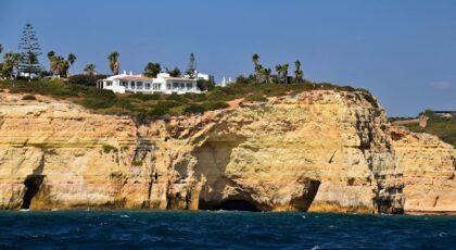 A stunning view of Algarve's sea cliffs with a villa on top, under a clear blue sky.