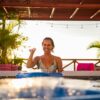 Smiling woman enjoying leisure time by a sunlit swimming pool in a villa.