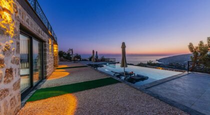 Serene coastal villa view with infinity pool and stunning sunset over the sea.