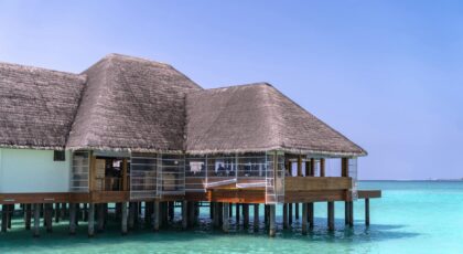 Stunning overwater bungalow with thatched roof on crystal-clear sea under bright blue sky, perfect for tropical vacations.