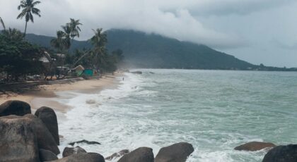 Serene view of a tropical beach in Koh Samui, Thailand, with crashing waves and lush greenery.
